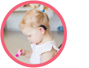 young girl with hearing aid looking down at a bubble blowing wand in her hand